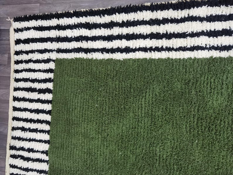 May include: A close-up of a textured rug with a green centre and a border of black and white stripes. The rug has a soft, plush appearance, suggesting a comfortable and decorative home textile.