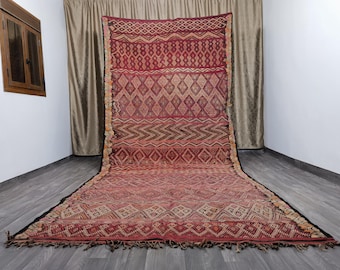 May include: A large, intricately woven rug with a geometric pattern in shades of red, brown, and cream. The rug has a fringe border and is laid out on a wooden floor.