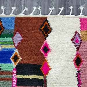 May include: A colorful Moroccan rug with a geometric pattern in shades of blue, green, pink, brown, and white. The rug has a fringe border.