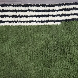 May include: A green and white striped rug. The rug has a textured, plush appearance. The top portion features thick, horizontal stripes in black and white. The bottom section is a solid, deep green colour.