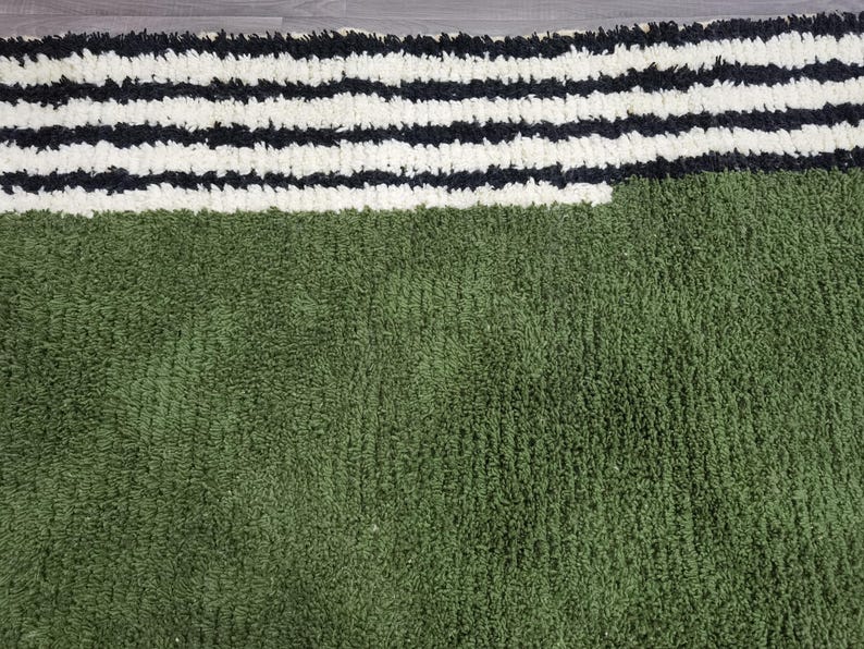May include: A green and white striped rug. The rug has a textured, plush appearance. The top portion features thick, horizontal stripes in black and white. The bottom section is a solid, deep green colour.