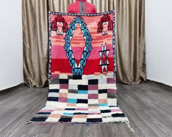 May include: A colorful Moroccan rug with a geometric pattern in shades of red, blue, pink, and white. The rug has a checkered pattern in the bottom half and a diamond-shaped pattern in the top half.