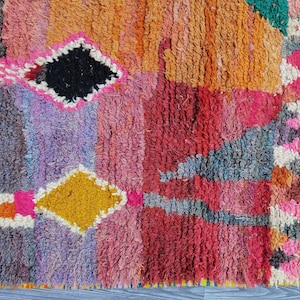 May include: A colorful Moroccan rug with a geometric pattern in shades of pink, red, orange, yellow, blue, and green. The rug has a textured, hand-woven look.