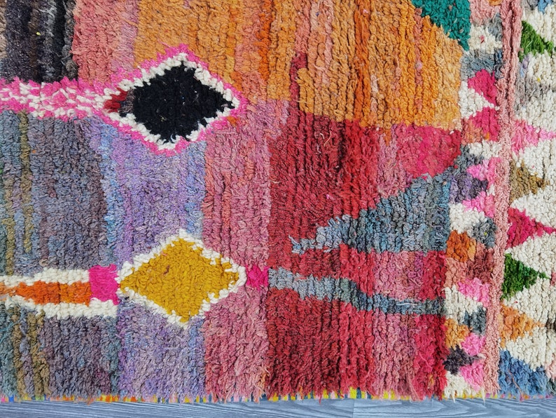 May include: A colorful Moroccan rug with a geometric pattern in shades of pink, red, orange, yellow, blue, and green. The rug has a textured, hand-woven look.