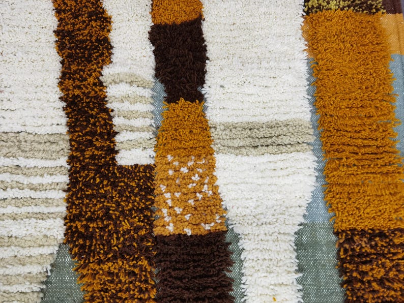 May include: Close-up of a textured rug with a repeating pattern of vertical stripes. The stripes are in shades of brown, white, tan, and gold. The rug has a soft, plush appearance, suggesting a comfortable texture.