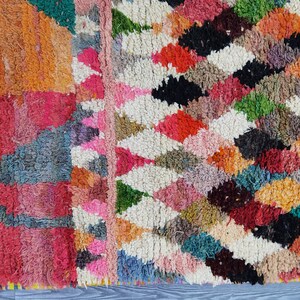 May include: Close-up of a colorful Moroccan rug with a geometric pattern. The rug is made of wool and has a variety of colors, including red, pink, orange, green, blue, and black.