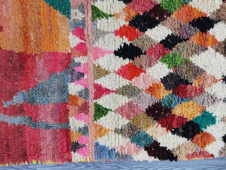 May include: Close-up of a colorful Moroccan rug with a geometric pattern. The rug is made of wool and has a variety of colors, including red, pink, orange, green, blue, and black.