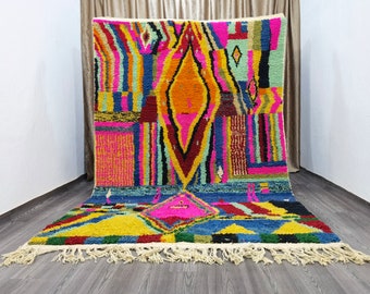 Könnte beinhalten: Ein bunter marokkanischer Teppich mit einem geometrischen Muster in den Farben Rosa, Blau, Gelb, Grün und Orange. Der Teppich hat einen Fransenrand.