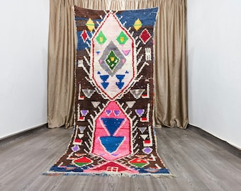May include: A colorful Moroccan rug with a geometric pattern in shades of pink, blue, green, and brown. The rug has a long, rectangular shape and is made of wool.