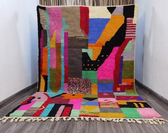 May include: A colorful Moroccan rug with geometric patterns in shades of pink, blue, green, orange, and black. The rug has a fringe border and is made of wool.