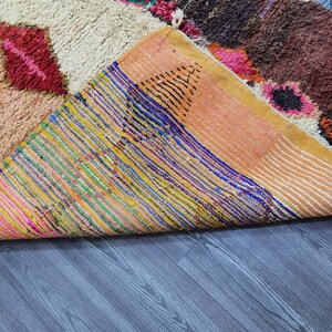 May include: A colorful Moroccan rug with a variety of patterns and textures. The rug is folded in half, revealing the underside, which is made of a woven fabric with a striped pattern.