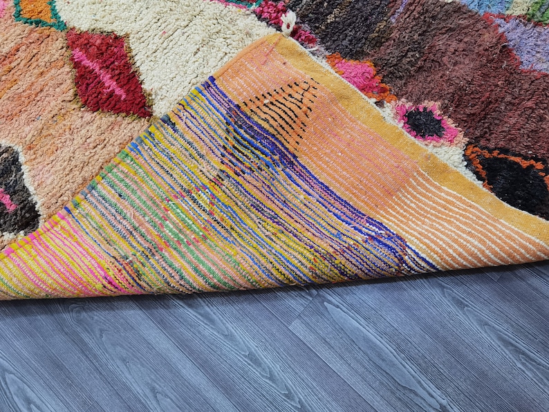 May include: A colorful Moroccan rug with a variety of patterns and textures. The rug is folded in half, revealing the underside, which is made of a woven fabric with a striped pattern.