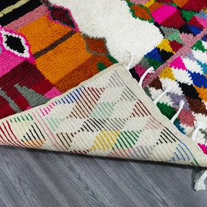 May include: A colorful Moroccan rug with a geometric pattern. The rug is made of wool and has a fringe border. The rug is folded in half and the underside is visible.
