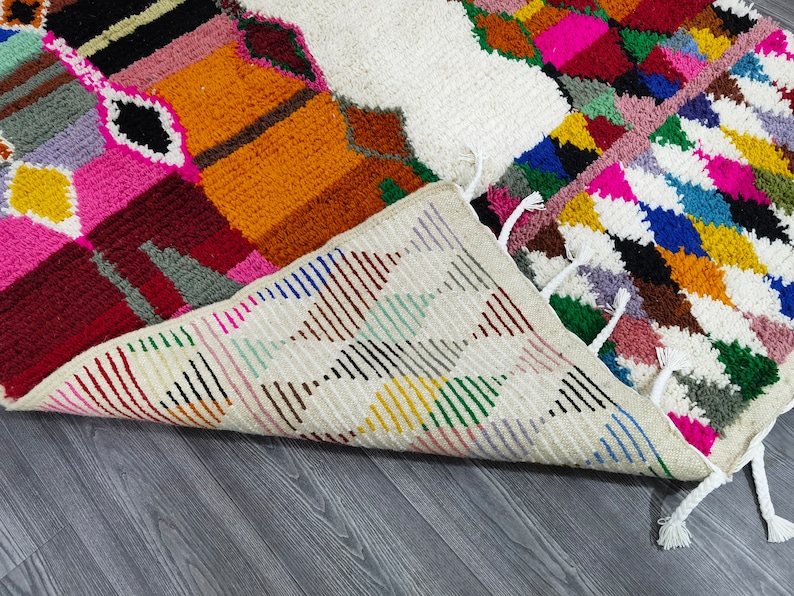 May include: A colorful Moroccan rug with a geometric pattern. The rug is made of wool and has a fringe border. The rug is folded in half and the underside is visible.