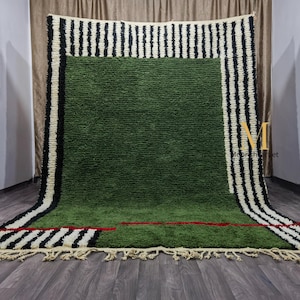 May include: A large, rectangular green rug with a textured surface. The rug features a border of alternating black and white vertical stripes. A red line accents the green field. The rug has a fringe along the bottom edge.