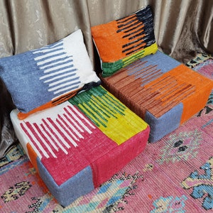 May include: Two colorful, patterned floor cushions with matching pillows. The cushions are made of a woven fabric with a variety of colors, including red, orange, yellow, green, and blue. The pillows are also made of woven fabric and have a similar pattern to the cushions.