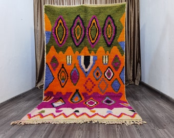 Könnte beinhalten: Ein farbenfroher marokkanischer Teppich mit einem geometrischen Muster in Orange-, Grün-, Rosa-, Blau- und Schwarztönen. Der Teppich hat einen Fransenrand und ist aus Wolle gefertigt.