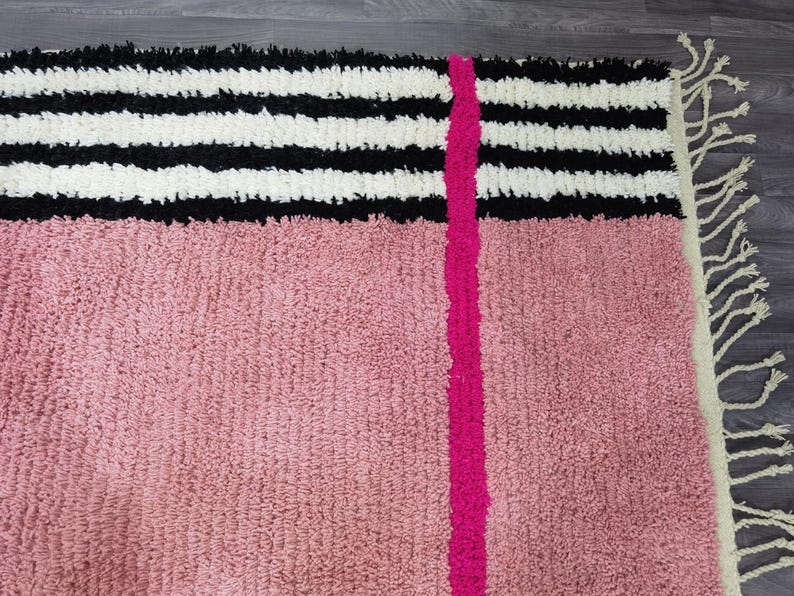 May include: A textured rug with a pink lower section and a black and white striped upper section. A bright pink vertical stripe runs down the center. The rug has a fringe on the right side.