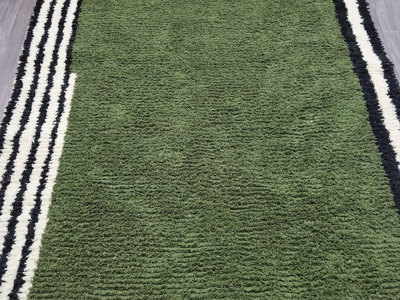 May include: A green rug with a textured surface. The rug has a border with black and white stripes on the left and right sides. The rug is made of a soft material.