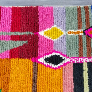 May include: A colorful, hand-woven rug with geometric patterns in shades of pink, red, orange, yellow, green, blue, and brown.
