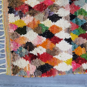 May include: A colorful Moroccan rug with a geometric pattern. The rug is made of wool and has a fringe border.