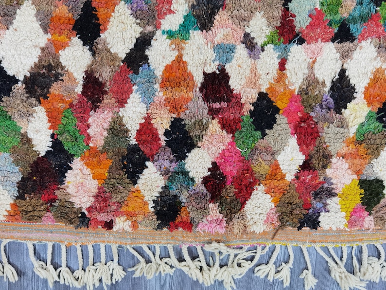 May include: A colorful Moroccan rug with a diamond pattern and fringe. The rug is made of wool and has a variety of colors, including red, orange, yellow, green, blue, and white.