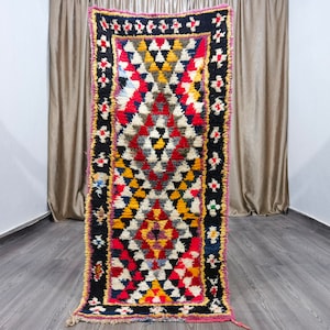 May include: A colorful Moroccan rug with a geometric pattern in shades of red, yellow, blue, black, and white. The rug has a fringe border.