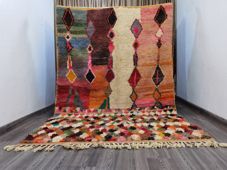 May include: A colorful Moroccan rug with a geometric pattern. The rug has a fringe border and is made of wool.