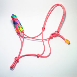 Puede incluir: Un cabezada de cuerda trenzada rosa con una bozal de cuerda trenzada arcoíris. La cabezada está hecha de paracord y está diseñada para caballos.