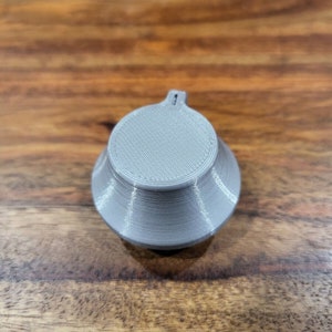 May include: A gray plastic knob with a textured surface and a small hole on top.