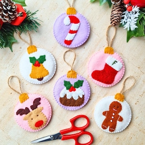 May include: Six circular felt Christmas ornaments featuring appliqued designs including a candy cane, a bell, a stocking with the letter F, a reindeer, a Christmas pudding, and a gingerbread man, each with a jute twine hanging loop.
