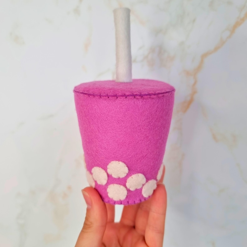 Puede incluir: Una taza de t&eacute; de burbujas de fieltro rosa con una pajita de fieltro blanco y perlas de boba de fieltro blanco.