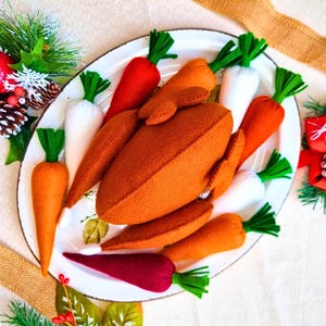 May include: A plush felt turkey centerpiece surrounded by several felt carrots in orange, white, and deep red colors. The turkey and carrots are arranged on a white oval platter with a dark rim, creating a decorative display for a holiday table.
