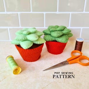 May include: Two felt succulent plants in red pots with green leaves. A spool of green thread, a spool of brown thread, and orange-handled scissors are also present. The text "PDF SEWING PATTERN" is at the bottom.