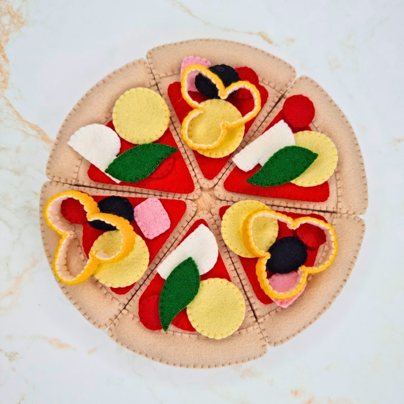 May include: A felt pizza toy consisting of six individual triangular slices arranged in a circle. Each slice features a tan crust, a red sauce base, and various felt toppings including yellow circles, green leaves, black circles, and orange rings.