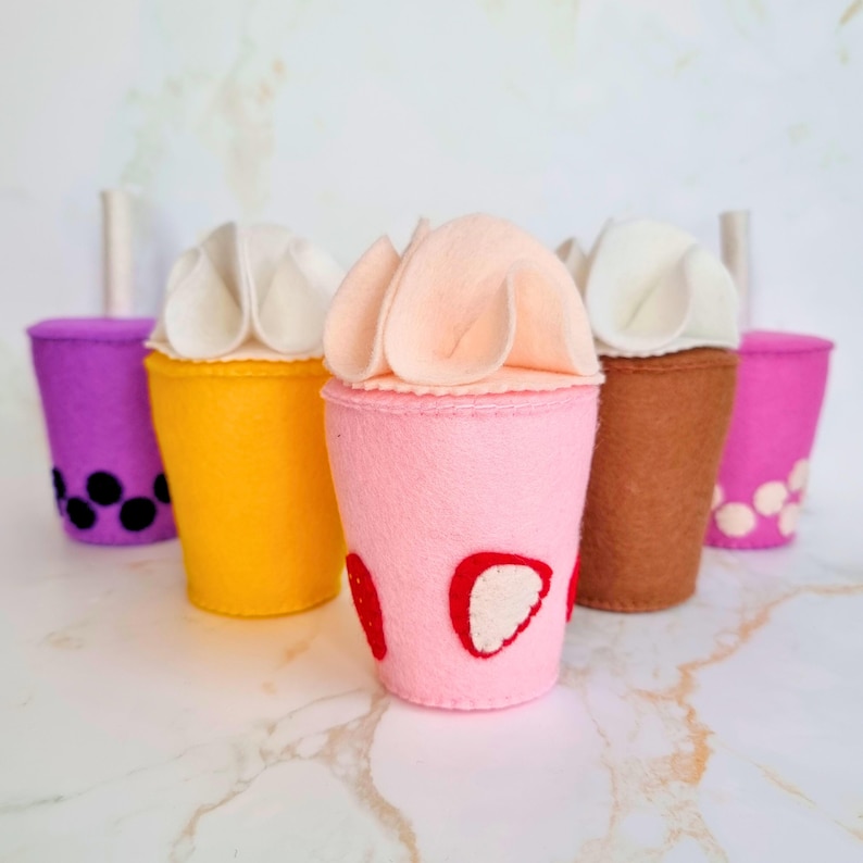 Puede incluir: Cinco vasos de t&eacute; de burbujas de fieltro con tapas de crema batida. Los vasos son morado, amarillo, rosa, marr&oacute;n y rosa. Los vasos rosas tienen dise&ntilde;os de fresa y boba. El vaso amarillo tiene dise&ntilde;os de boba. El vaso marr&oacute;n tiene dise&ntilde;os de boba. El vaso morado tiene dise&ntilde;os de boba.