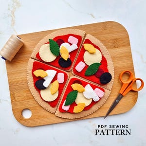 May include: A felt pizza toy with four removable slices, each topped with colourful felt ingredients like olives, mushrooms, and basil. The pizza sits on a wooden cutting board, with scissors and thread nearby. The text "PDF SEWING PATTERN" is at the bottom.