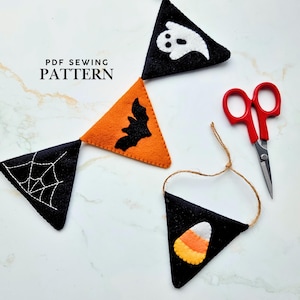 Op de afbeelding: Een PDF-naaipatroon met vier driehoekige viltwimpels met Halloween-motieven, waaronder een wit spook, een zwarte vleermuis, een wit spinnenweb en een candy corn, vergezeld door een rode schaar.