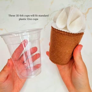 Puede incluir: Una taza de fieltro marr&oacute;n con glaseado de fieltro blanco en la parte superior. La taza de fieltro se muestra junto a una taza de pl&aacute;stico transparente de 12 oz. "Estas tazas de fieltro 3D se ajustan a las tazas de pl&aacute;stico est&aacute;ndar de 12 oz" est&aacute; escrito en la imagen.