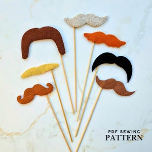 May include: A selection of felt moustache props in shades of brown, black, orange, and grey, mounted on wooden sticks. The text "PDF SEWING PATTERN" is visible. These props are likely for photo booths or crafting projects.