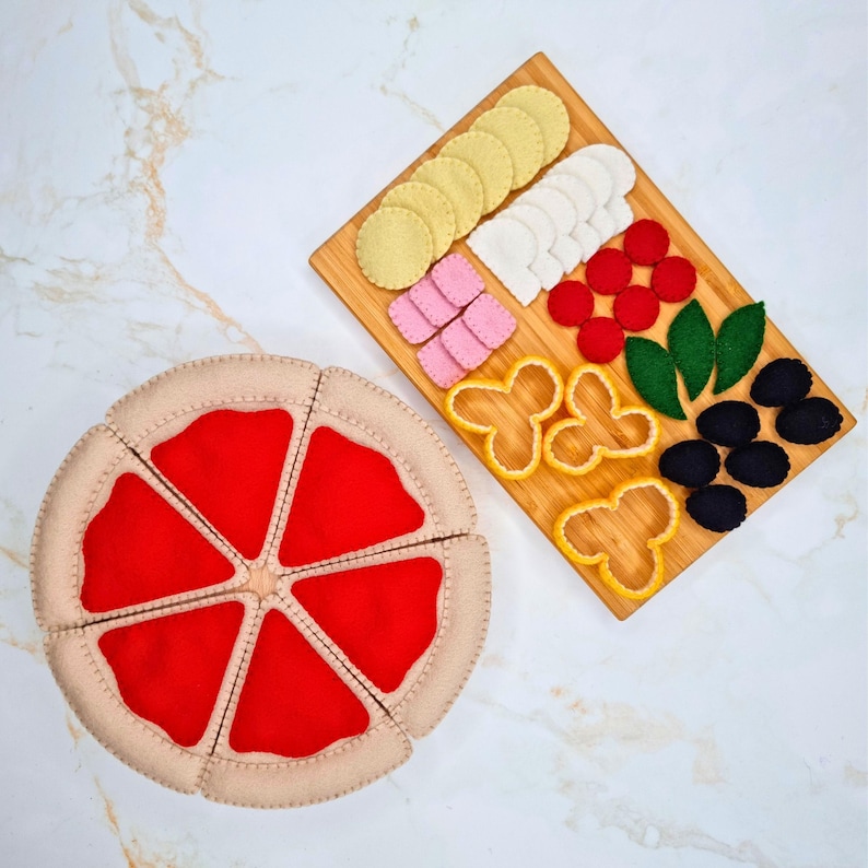 May include: A felt pizza toy set consisting of six beige crust slices with red sauce centers, accompanied by a rectangular wooden board featuring various felt toppings including yellow circles, white semicircles, red circles, pink squares, green leaves, and black ovals.