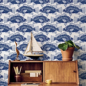 May include: A wooden desk with drawers and a chair is set against a wall covered in a repeating pattern of blue fish on a white background. Decorative items include a model sailboat, a small wooden bird, and a potted plant.