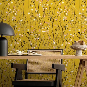 May include: A mustard yellow floral wallpaper with black branches and white and pink flowers. A wooden desk with a black chair, a black lamp, and decorative items. The room has a modern, minimalist aesthetic.