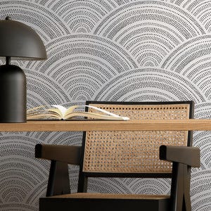 Puede incluir: Un escritorio en casa con un escritorio de madera, una silla negra con respaldo tejido y una lámpara negra. El fondo es un papel pintado con un patrón repetitivo de puntos negros en diseño de abanico. Un libro y un cuenco decorativo están sobre el escritorio.