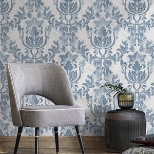 May include: A room scene featuring a gray upholstered chair with black legs and gold accents. The background is a wallpaper with a blue and white damask pattern. A gold planter with a green plant is on the left.