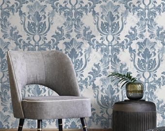 May include: A room scene featuring a gray upholstered chair with black legs and gold accents. The background is a wallpaper with a blue and white damask pattern. A gold planter with a green plant is on the left.