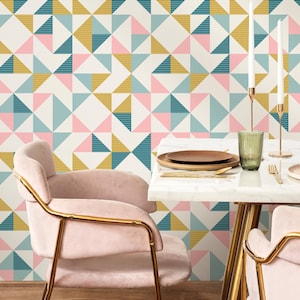 May include: A dining room setting with a table and chairs. The table has a white marble top and gold legs. Two pink velvet chairs with gold frames are at the table. The background features geometric wallpaper in pink, teal, and gold.