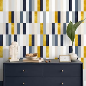 May include: A navy blue dresser with gold knobs is set against a wallpaper with vertical stripes in gold, navy, gray, and white. A white sculpture, a small clock, and a vase with a green leaf are on top of the dresser.