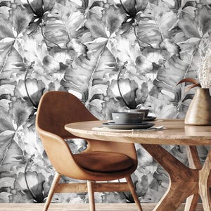May include: A dining room scene with a round wooden table and a brown leather chair. The background is a black and white floral wallpaper. A vase with dried flowers and two bowls are on the table.