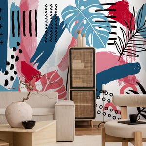 Könnte beinhalten: Ein modernes Wohnzimmer mit einem abstrakten Wandbild im Hintergrund. Das Wandbild zeigt blaue, rote und rosa Pinselstriche und Blattmotive. Der Raum umfasst ein beiges Sofa, einen Holztisch, einen gewebten Schrank und einen beigen Teppich.